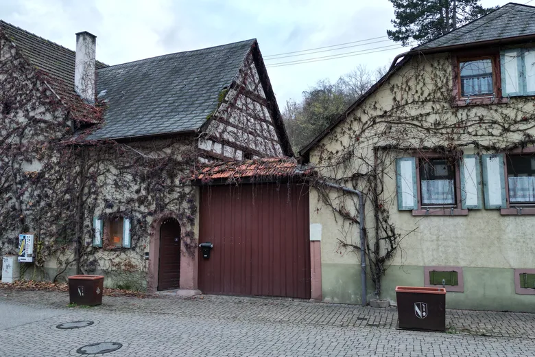 Efeubewachsenes Altbau-Anwesen mit Fachwerkgiebel und Scheunentor an einer Dorfstraße.