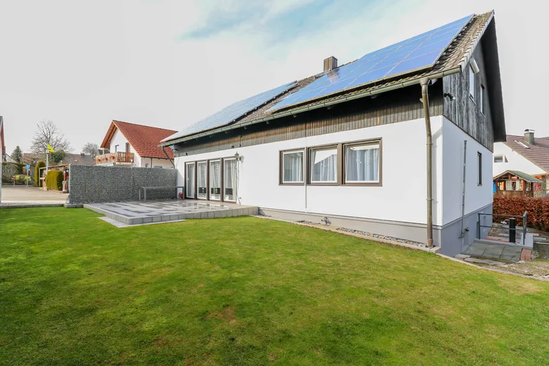 Weißes Zweifamilienhaus mit Photovoltaik auf dem Dach und großem Rasengrundstück.