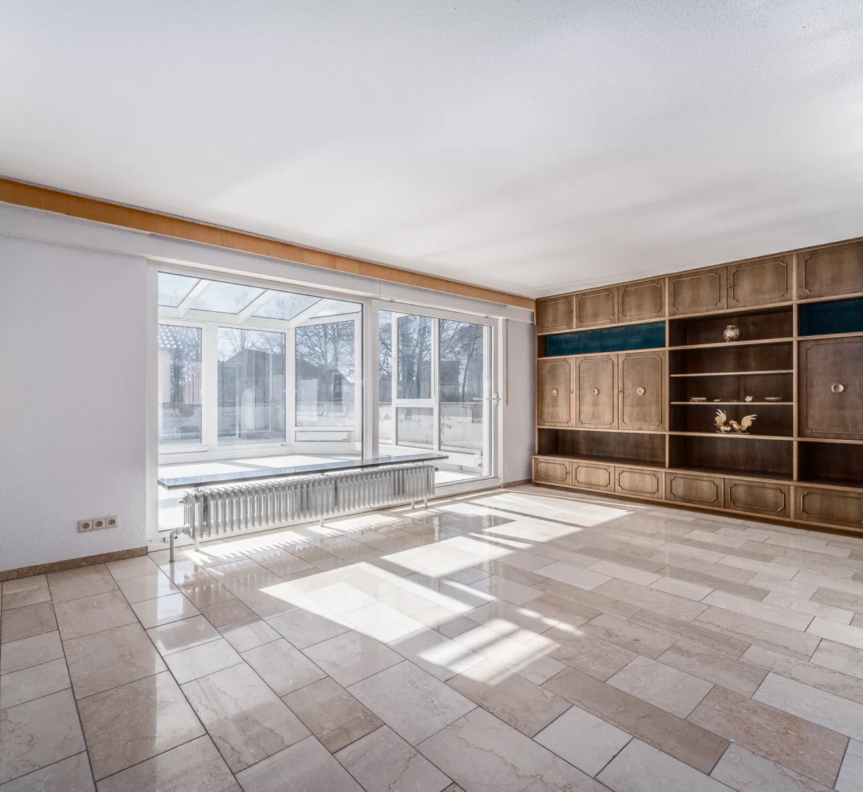 Leerer Wohnraum mit Einbauschrankwand und Fensterfront zum Wintergarten